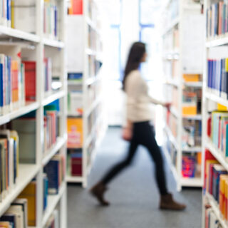 Frau geht durch Bücherregale in einer Bibliothek